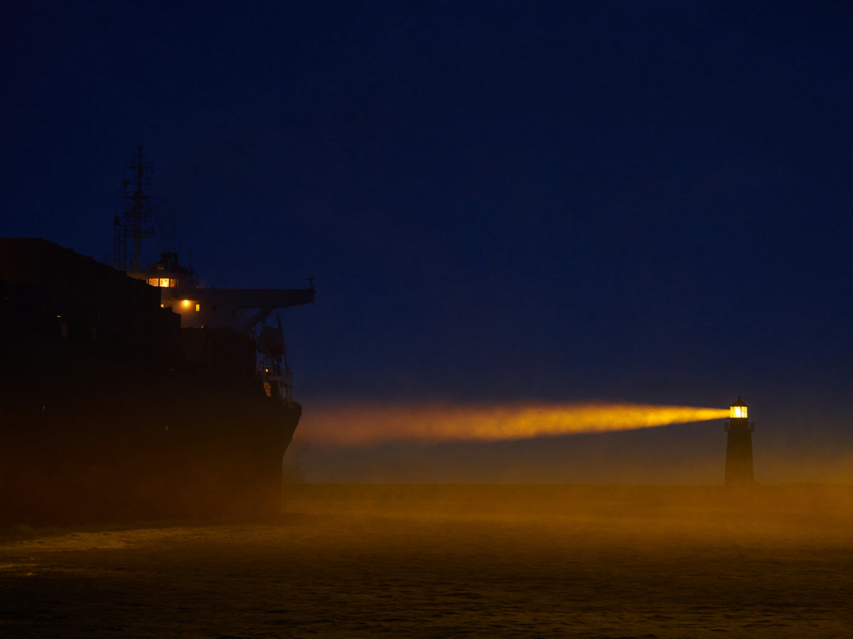 Navio de carga guiado pelo facho de um farol ao entrar no porto